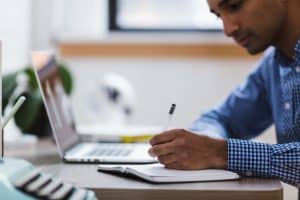 an outsourced employee doing research on a computer and writing it on a notepad