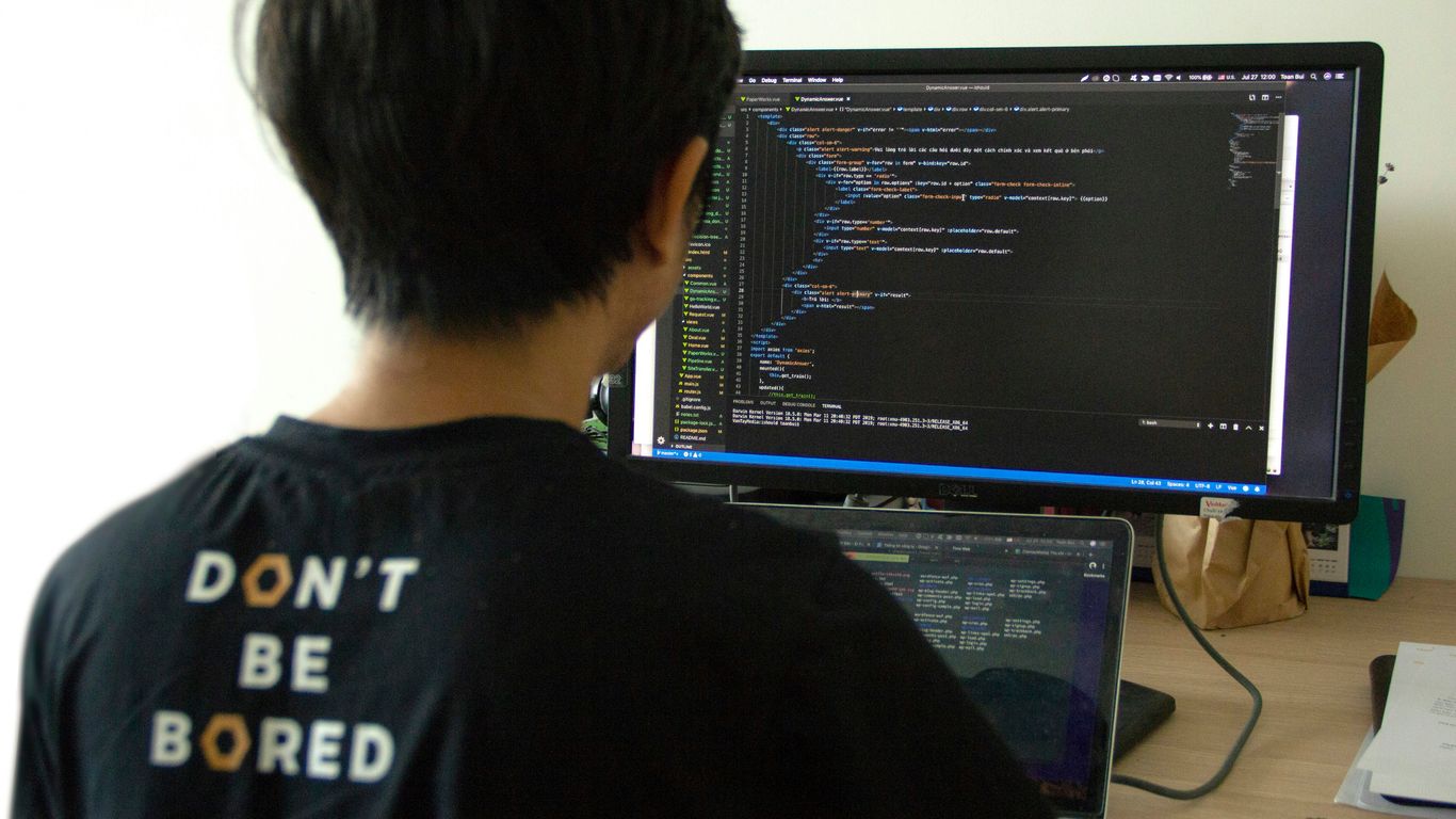 man in black shirt using laptop computer and flat screen monitor