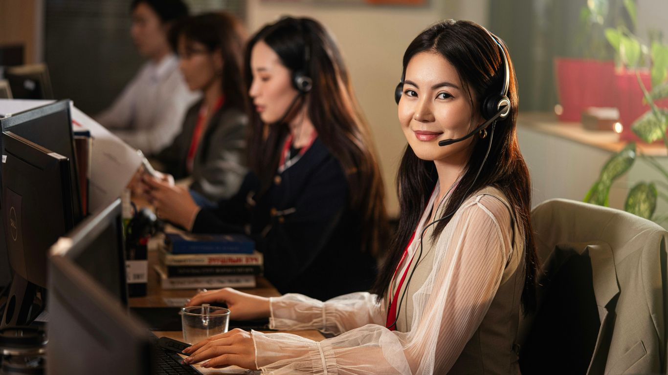 A smiling woman wearing a headset at a computer.