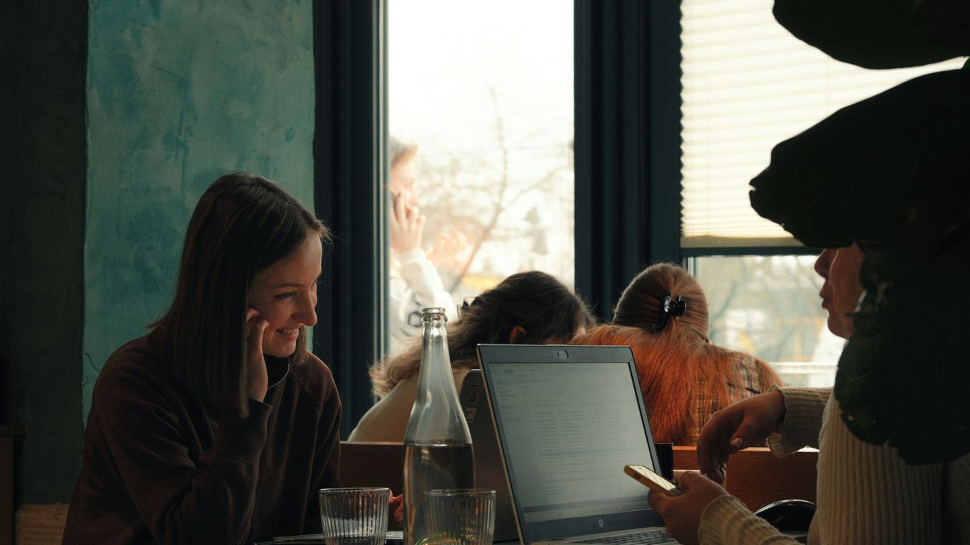 Two women talk at a table with a laptop.