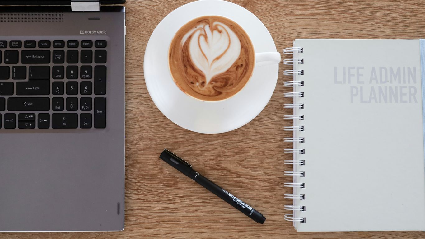 a cup of coffee on a saucer next to a laptop