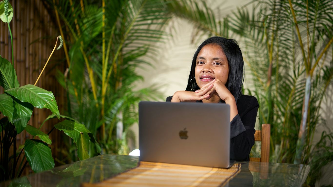 Young woman working on a laptop surrounded by plants.