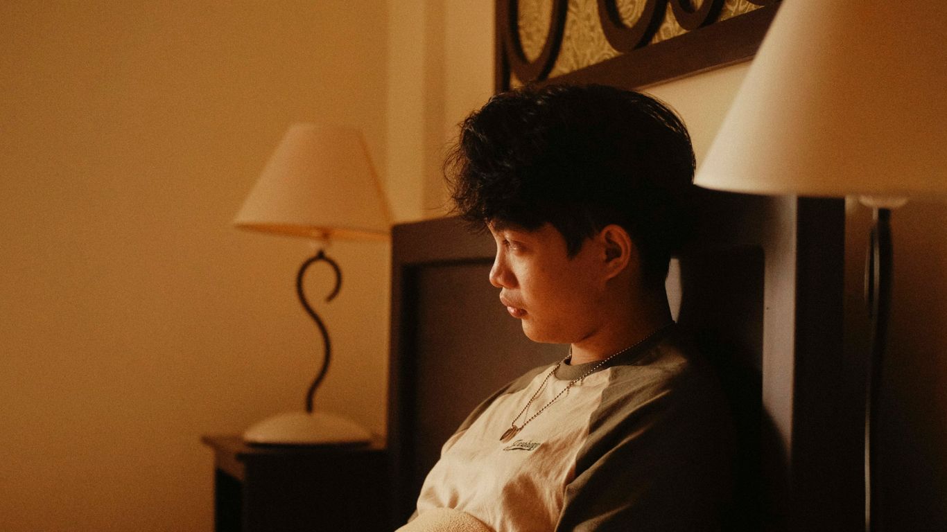 a young man sitting on a bed in a hotel room